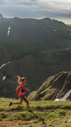 a woman running up a hill with mountains in the background