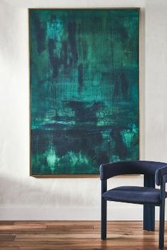 a blue chair sitting in front of a large green painting on the wall next to a wooden floor