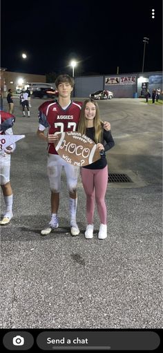 two people standing next to each other with a football sign in front of the camera