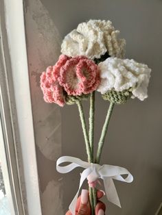 a person holding three flowers in their hand with ribbon around the stems, and another flower that has been crocheted on it