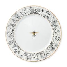 a white and black plate with a bee on the center, surrounded by flowers in gold trim