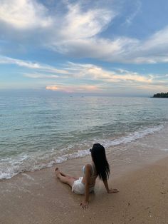 a woman sitting on top of a sandy beach next to the ocean under a cloudy sky