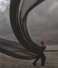 a woman standing on top of a sandy beach next to a black and white kite