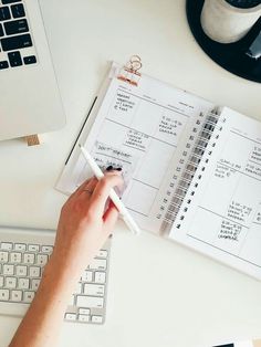 a person is writing on a planner next to a laptop