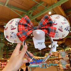 a person holding up a minnie mouse ears with red and black plaid bow on it