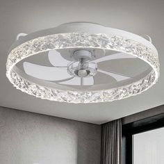 a white ceiling fan with crystal accents in a living room or dining room, next to a window