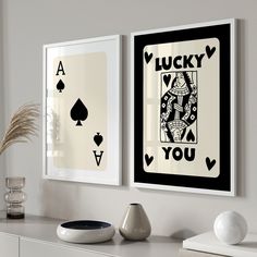 two framed playing cards hang on the wall next to a vase with some plants in it