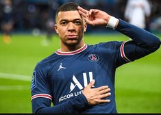 a soccer player saluting on the field with his hand up to his ear and looking at the camera