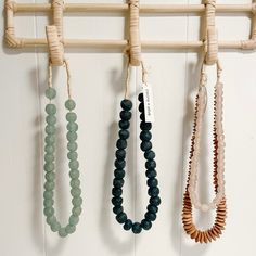 three necklaces hanging from a wooden rack on a white wall next to other beads