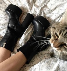 a cat sitting on top of a bed next to a woman's legs and boots