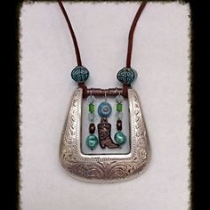 a silver necklace with glass beads and a cat on the front is hanging from a brown cord