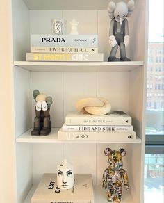 some books and figurines are on top of the shelves in this white room