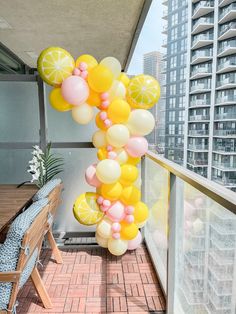 a bunch of balloons that are on the side of a building near a table and chairs