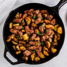 a skillet filled with meat and potatoes on top of a white tablecloth next to a