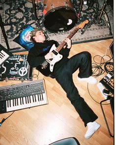 a man laying on the floor with his guitar in front of him and musical equipment around him