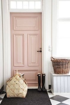 a pink door with black and white checkered flooring next to a basket on the ground