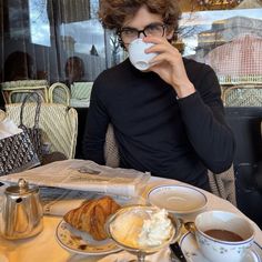 a man sitting at a table drinking coffee and eating croissants