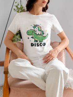 Get the party started with our magical Unicorn Riding Dinosaur T-Shirt! This whimsical tee features a vibrant and colorful print of a unicorn proudly perched atop a friendly dinosaur, set against a starry night background with the word 'DISCO' in bold, fun lettering. Perfect for anyone who loves to mix fantasy with a touch of humor. Made with high-quality materials, this shirt is comfortable for all-day wear and is a great conversation starter at parties or casual hangouts. Available in a variet Starry Night Background, Fun Lettering, Mythical Creature, Cool Lettering, Top Funny, Disco Party, Top Tee, Solid Black, Length Sleeve