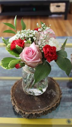 a vase filled with pink and red flowers on top of a wooden table next to a tv