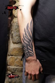 a man's arm with a black and grey wing tattoo on his left arm