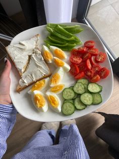 a person holding a plate with vegetables and eggs on it, including cucumbers