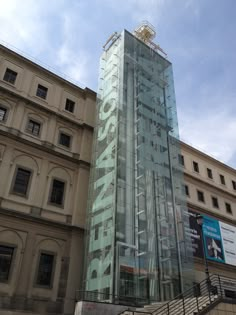 a tall glass building sitting in front of a large building with stairs leading up to it