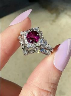 a close up of a person's hand holding a ring with a pink manicured nail