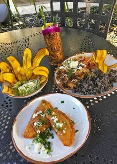 three plates with food on them are sitting on a table near bananas and other foods