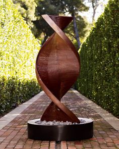 a sculpture is shown in the middle of a brick path with trees and bushes behind it