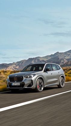 a silver bmw suv driving down the road in front of mountains and desert area with blue sky