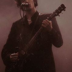 a man with curly hair holding a guitar and singing into a microphone while standing in front of a microphone