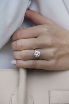 a woman's hand with a diamond ring on her left hand, holding a beige purse