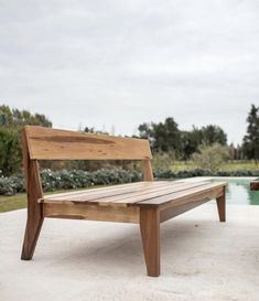 a wooden bench sitting on top of a cement floor next to a pool with trees in the background