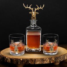 two glasses and a decanter on a wooden tray with a deer head in the top