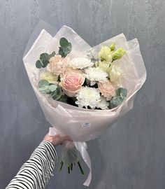 a woman holding a bouquet of white and pink flowers with greenery in it's hands