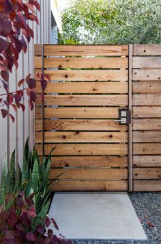 a wooden gate in the middle of a yard with gravel and plants on either side