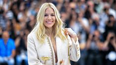 the blonde woman is smiling and holding her hand up to her face as she stands in front of a large group of people