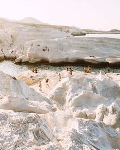 many people are swimming in the water near some white rocks and icebergs that look like they have been frozen