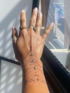 a woman's hand with tattoos and rings on her left wrist, next to a window