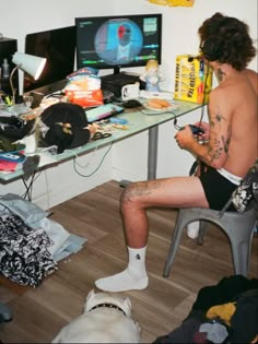 a shirtless man sitting in front of a computer desk with a dog on the floor