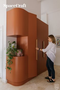 a woman is standing in front of a cabinet with plants on it and holding the door open