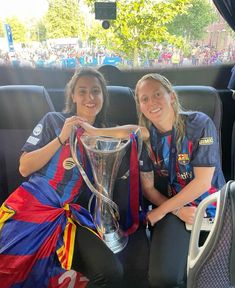 two women sitting in the back of a car holding up a soccer trophy and posing for a photo