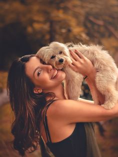 a woman holding a small white dog in her arms and smiling at the camera while she holds it up