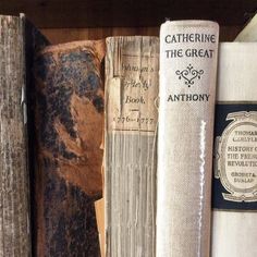 an old book is sitting on top of a wooden shelf with other books behind it