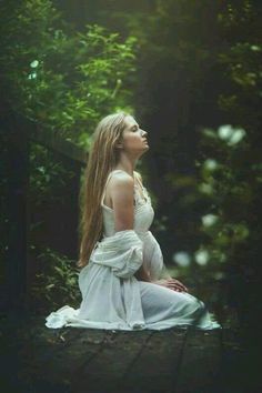 a woman in white dress sitting on the ground with her eyes closed and looking up