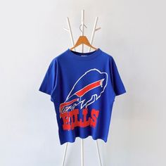 90s Buffalo Bills NFL t-shirt/ L * PLEASE READ BEFORE PURCHASE * PLEASE consider the PHOTOS before making the decision * The images may DIFFER in appearance from the actual product because we took pictures under daylight.  * PLEASE send your PHONE NUMBER after your purchase for the shipping company to contact you X No returns X No refund Condition : 9/10 More details : look at the pictures  Brand : Apex one Size : L Pit to pit/ Chests : 23.5/47 inches  Length : 28.5 inches  Material : cotton  Color : blue * ALL ITEMS are VINTAGE which may show some signs of wear and tear * Due to the different display and different light, the picture may not reflect the actual color of the item * Please, remember that our items are vintage so they may show some signs of wear, tear and yellow stains. Thank 90s Inspired Short Sleeve T-shirt With Screen Print, 90s Inspired Short Sleeve T-shirt For Fans, 90s Inspired Blue T-shirt With Letter Print, Bills Sweatshirt, Buffalo Bills Shirts, 90s Blue T-shirt With Text Print, Vintage Bills Sweatshirt, Buffalo Bills Sweatshirt, Buffalo Bills Vintage Sweatshirt