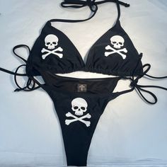 This black bikini has three hand printed skull & cross bones designs, branded with an AcidCore label.    It features V-strings for the bottom and a comfortable triangle-style wireless bra with a halter neckline.  The fabric is of high stretch quality, and care instructions recommend machine washing while avoiding dry cleaning. Additionally, the bikini includes removable padding for the chest and is composed of 80% Polyamid 20% Elastane. Both the bikini top and bottom are lined for added comfort. Grunge Swimsuit, Skull Bra, Cross Bones, Wireless Bra, Halter Neckline, Favorite Outfit, Bathing Beauties, My Style, Music Clothes