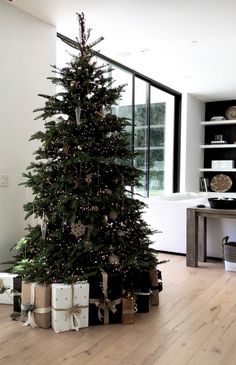 a christmas tree with presents under it on the floor in front of a large window