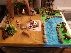 a wooden table topped with lots of fake rocks and animals next to a lit candle