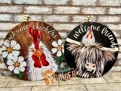 two wooden signs with roosters and daisies on them are sitting against a brick wall